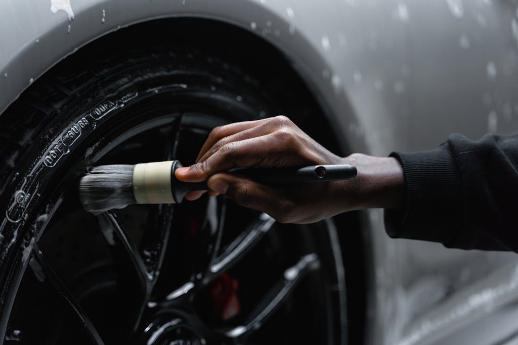 A detail-oriented close-up of a hand cleaning a car tire with a brush and soap.