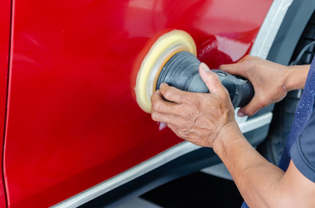 Close-up of a worker buffing red car paint for shine and maintenance.